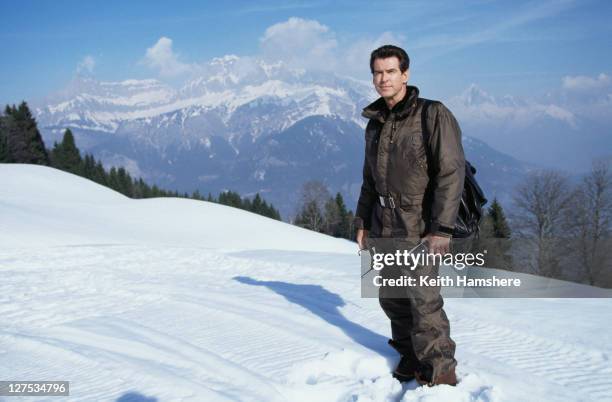 Irish actor Pierce Brosnan on location in France for the skiing sequence of the James Bond film 'The World Is Not Enough', 1999. He is holding a copy...