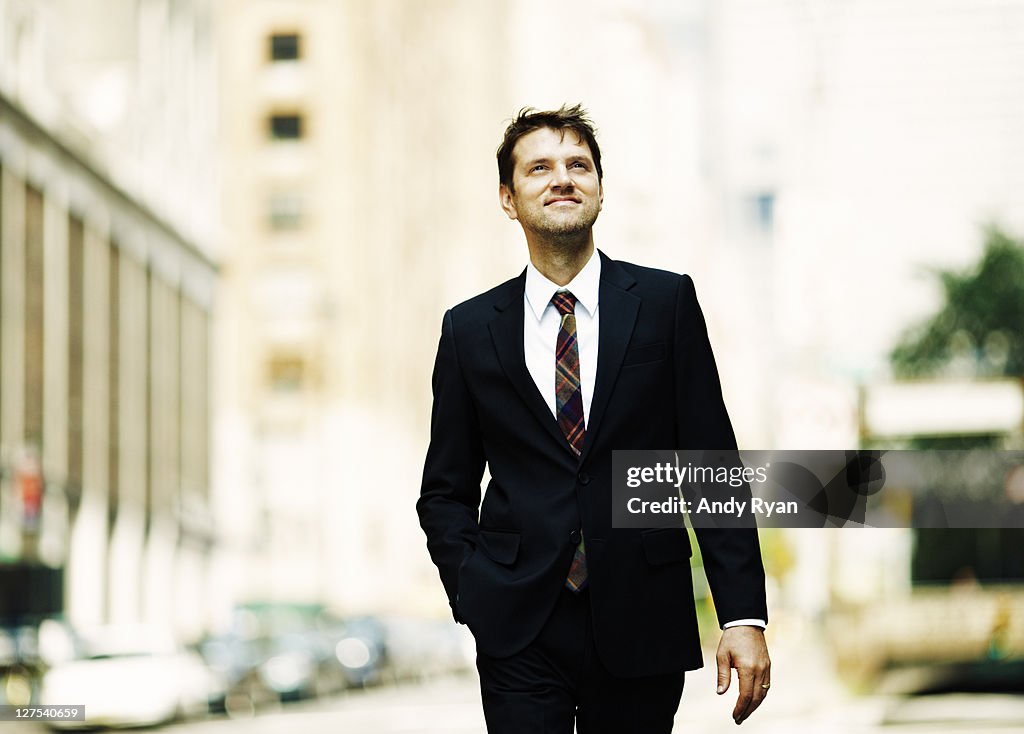 Businessman walking on city street, looking upward