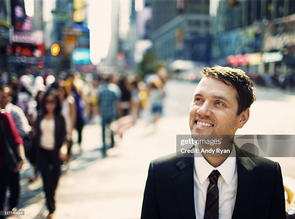 Smiling businessman in city, looking up.