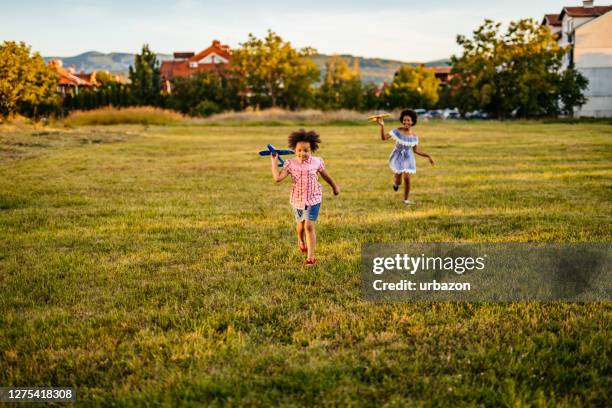 girls are playing with airplane toys in field - perseguir ir atrás de imagens e fotografias de stock