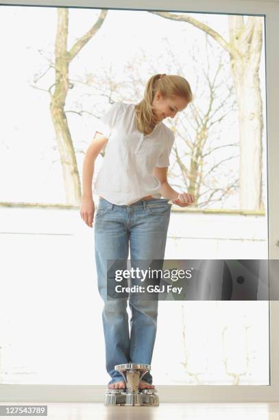 woman wearing large jeans on scale - satisfaction scale stock pictures, royalty-free photos & images