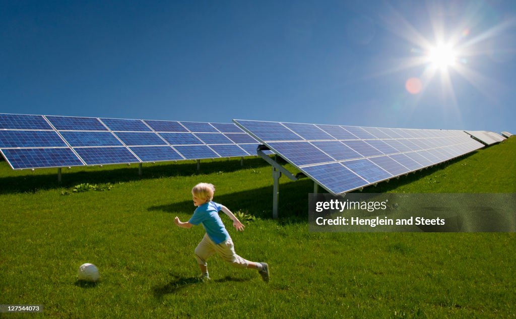 Boy playing in field by solar panels