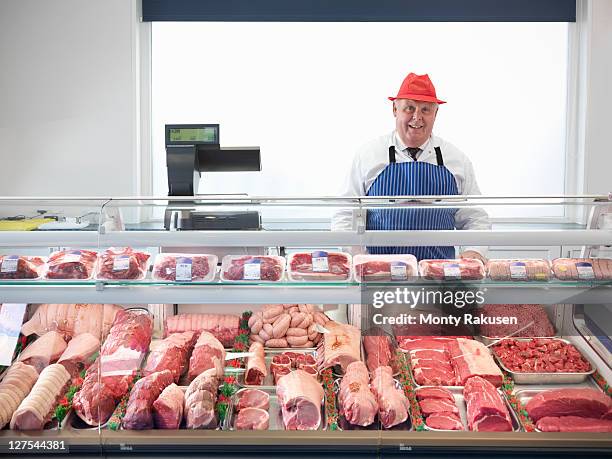 butcher standing behind meat counter - macellaio foto e immagini stock