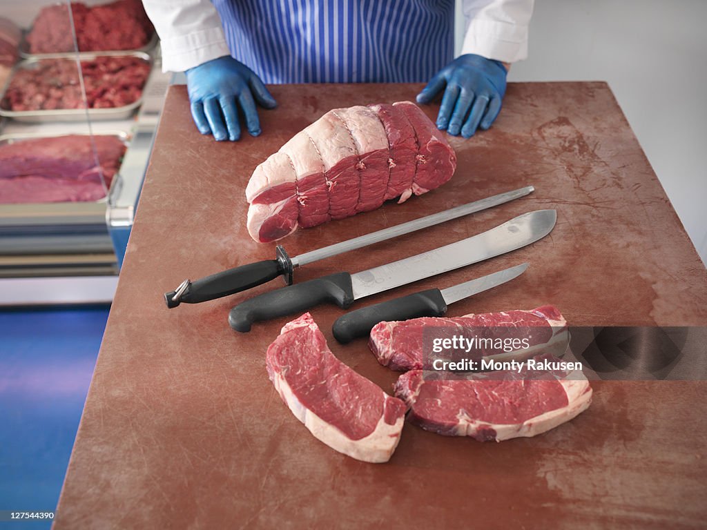 Butcher with knives and cuts of pork