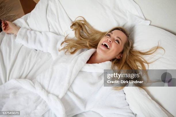 smiling woman laying on bed - bathrobe stock pictures, royalty-free photos & images