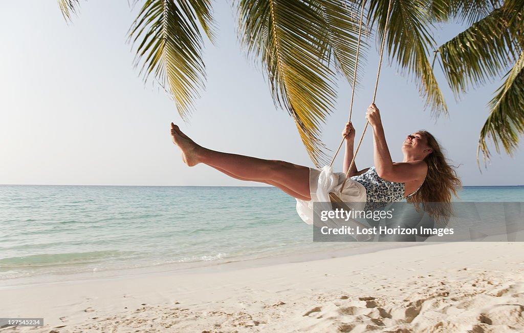 Smiling woman swinging on tropical beach