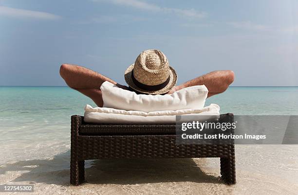 man relaxing on daybed at tropical beach - sdraio da spiaggia foto e immagini stock