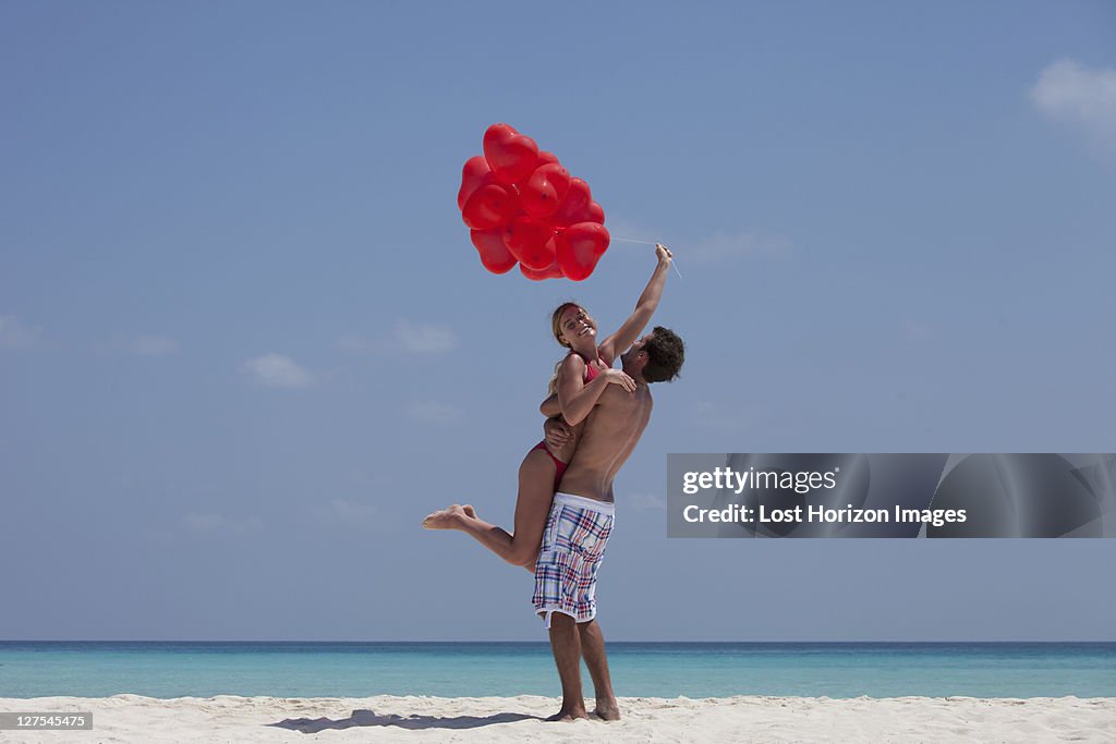 Couple hugging with balloons on beach