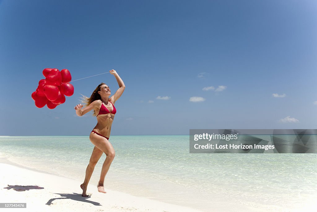 Woman running with balloons on beach