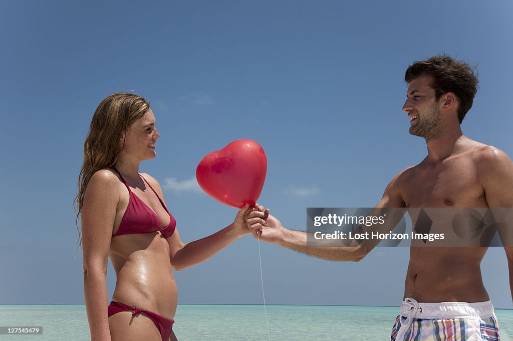 Casal partilha balão vermelho na praia