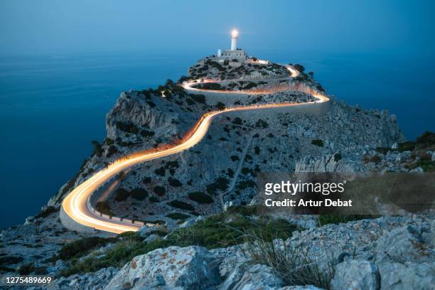 car light trails in curvy road with lighthouse and extreme terrain in the north of mallorca island. - light natural phenomenon stock pictures, royalty-free photos & images