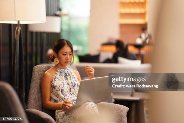 young asian business woman wearing casual dress sitting at luxury hotel lobby using laptop to working - vertrekhal stockfoto's en -beelden