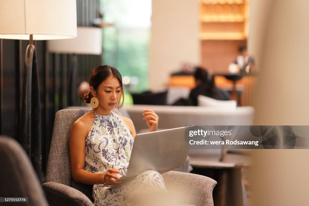 Young Asian business woman wearing casual dress sitting at luxury hotel lobby using laptop to working