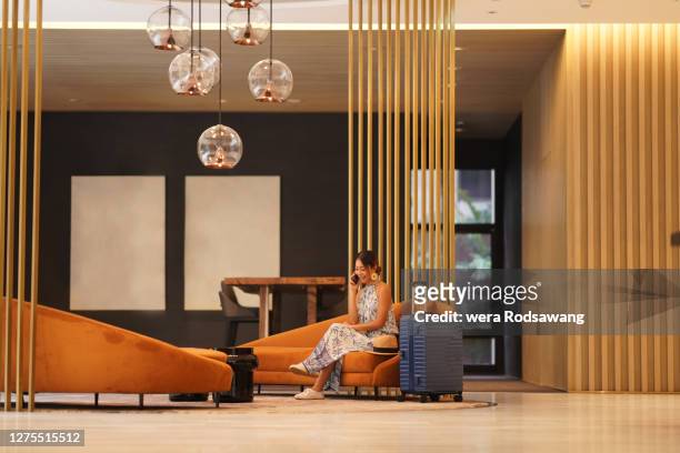 young tourist woman sitting on sofa at hotel lobby lounge using phone to talking and smiling - lobby stock pictures, royalty-free photos & images