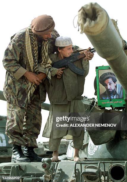 Northern Alliance soldier teaches a young boy how to hold Kalashnikov, standing on a tank of his regiment, with the portrait of assassinated Afghan...