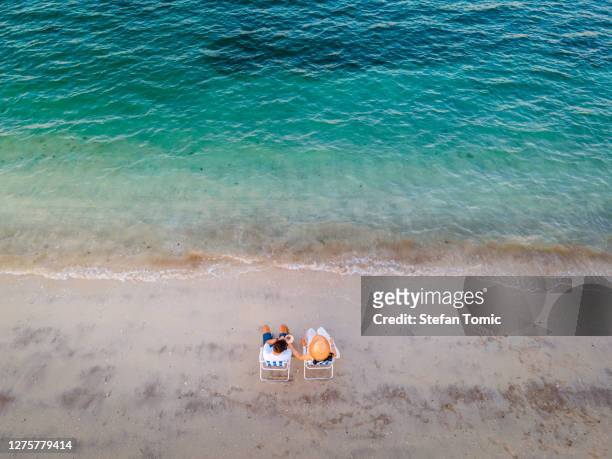 couple enjoying on the beach sitting on the tanning chairs at sunset - coconut beach woman stock pictures, royalty-free photos & images