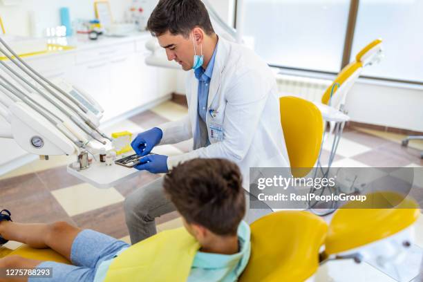 dentist examining boy's teeth in clinic - dentist covid stock pictures, royalty-free photos & images
