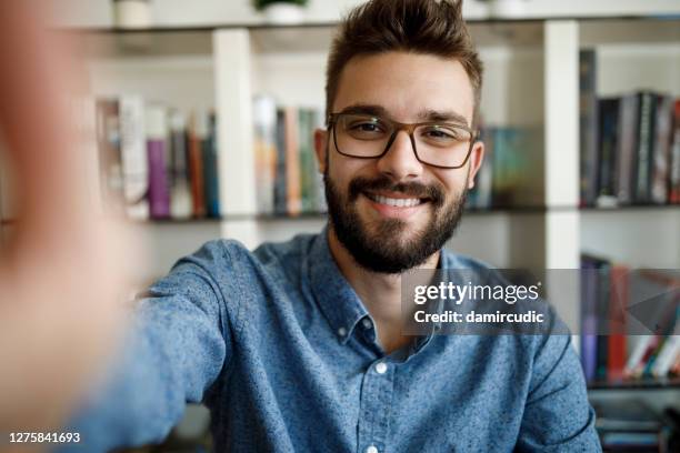 jeune homme de sourire ayant la conférence en ligne de la maison - webcam photo photos et images de collection