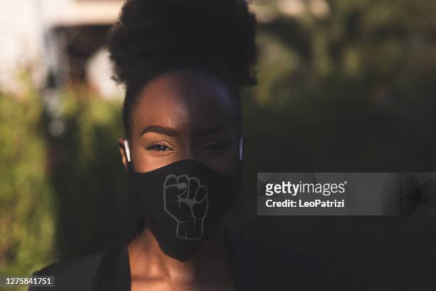 woman wearing a black face mask with a fist printed on it - anti racism stock pictures, royalty-free photos & images