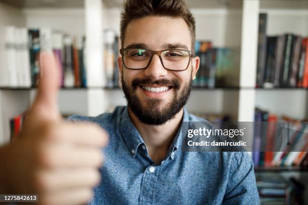 kameraansicht eines jungen mannes mit daumen nach oben im home office - mann lachen blick in die kamera stock-fotos und bilder
