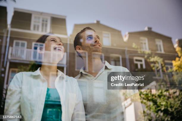 young couple in their new home looking out of the window - netherlands windows stock pictures, royalty-free photos & images