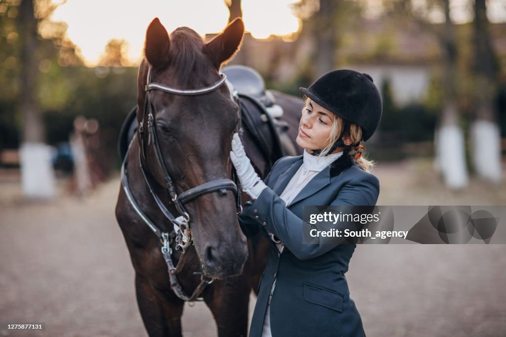 Bellissimo fantino femminile che abbraccia il suo cavallo dopo l'allenamento al maneggio