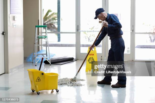 senior adult janitor dweilt vloer bij binnenkomst in kantoren. - schoonmaker man stockfoto's en -beelden