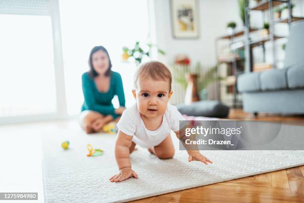 mutter und baby mädchen zu hause, baby kriechen und auf der suche nach spielzeug - crawling stock-fotos und bilder