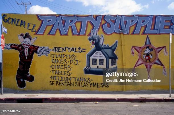 Gonzalez Party Supplies on San Pedro Street in Los Angeles, California has a mural showing a clown, a bounce house, and a Mickey Mouse pinata painted...