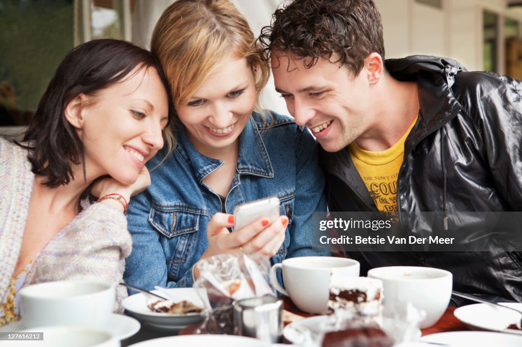 Group of friends looking at photos/ phone in cafe