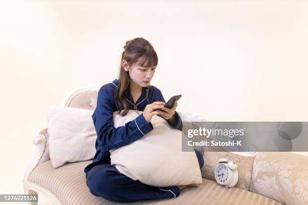 young woman in pajama sitting on couch and using smart phone - sitting and using smartphone studio stock pictures, royalty-free photos & images