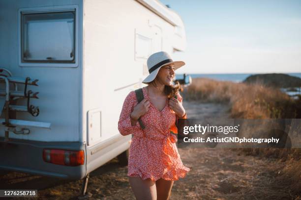 woman with a straw hat and backpack is walking next to her camper - camping bus stock pictures, royalty-free photos & images