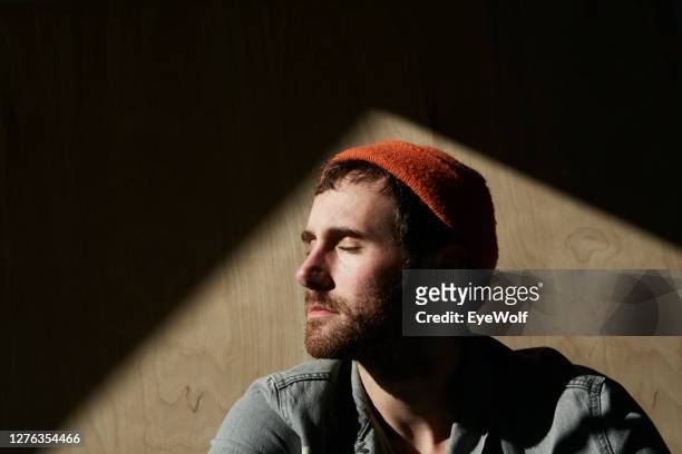portrait of a man sitting in sunlight against a wooden background. - alto contraste imagens e fotografias de stock