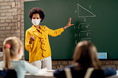 Black teacher wearing face mask while explaining math lesson in the classroom.