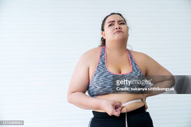 overweight woman measuring her waist size with tape measure and feel stressed by her weight gain. - fat woman stock-fotos und bilder