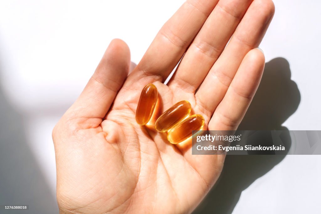 Woman's hand holding fish oil supplements on white background.