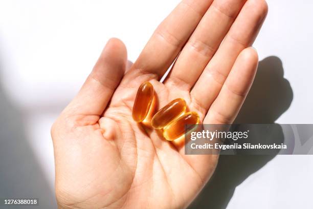 woman's hand holding fish oil supplements on white background. - omega 3 stock pictures, royalty-free photos & images