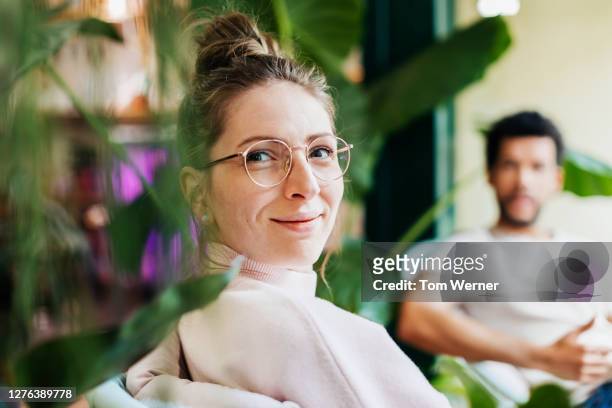 portrait of woman sitting between plants in café - messa a fuoco differenziale foto e immagini stock