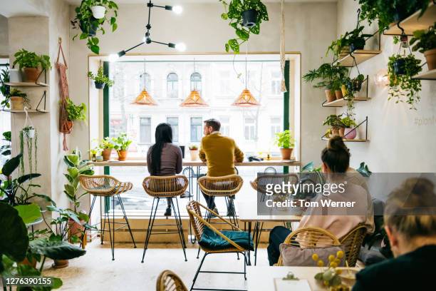 couple sitting in front of window in quirky café - leben in der stadt stock-fotos und bilder