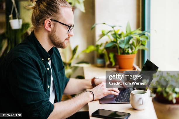 man working on laptop in local café - blond undone stock-fotos und bilder