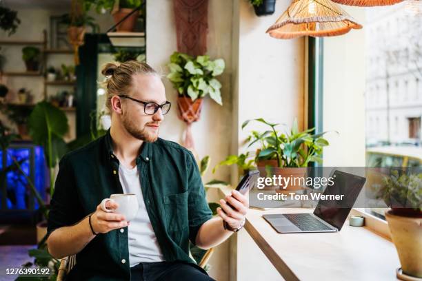 student using smartphone while drinking coffee - blonde glasses foto e immagini stock