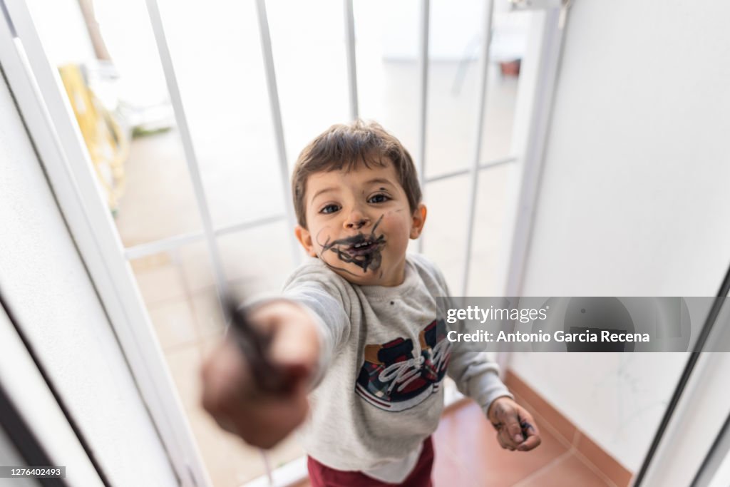 Little baby boy showing crayon to his father after painting a black face