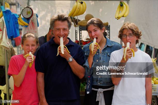 Dustin Hoffman and Daughters, Allie and Becky, and son, Max, posed in front of a Fruit stand on Columbus Avenue and 72nd Street and biting into...