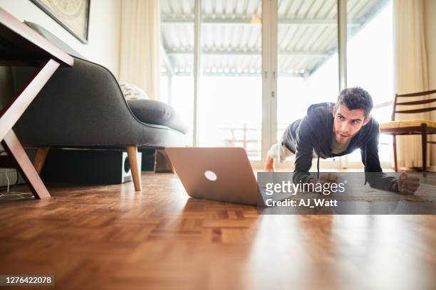 jonge mens die tijdens een online training in zijn woonkamer planking - man doing yoga in the morning stockfoto's en -beelden