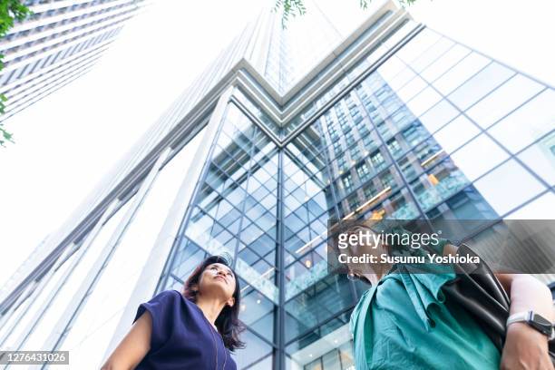 two businesswomen looking up at a building in town - japanese bussiness woman looking up stock-fotos und bilder