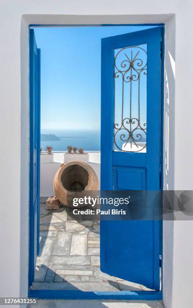 bright sun and a traditional pot seen throught a beautiful blue door in santorini, in the background caldera, - mediterranean-blue-roof-santorini stock pictures, royalty-free photos & images