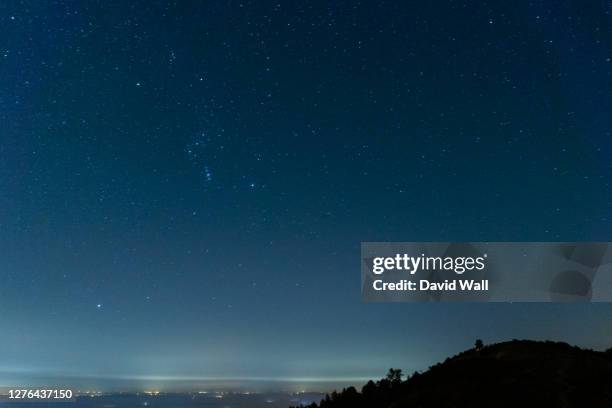 looking down on a town at night, covered in fog. with the night sky and the orion constellation above. - orionnebel stock-fotos und bilder