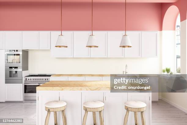 cocina amurallada rosa con armarios blancos, luces colgantes, isla de cocina y suelo de madera - isla de cocina fotografías e imágenes de stock