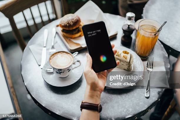 overhead view of young woman using ai assistant on smartphone while having a light meal in a coffee shop. enjoying a relaxing afternoon - speech recognition stock pictures, royalty-free photos & images