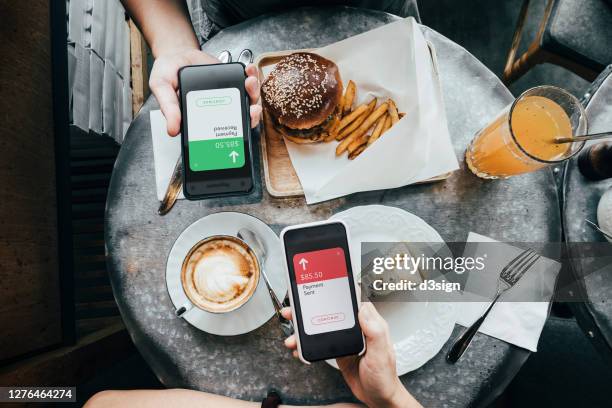 overhead view of friends sending/receiving the payment of the meal through digital wallet device on smartphone while dining together in a restaurant - phone payment stock-fotos und bilder